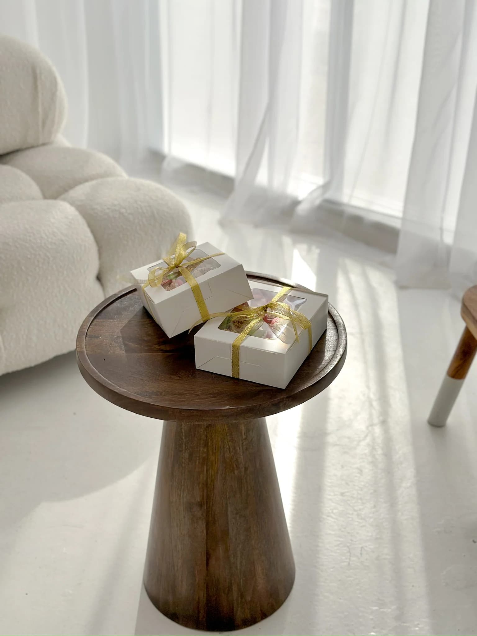 Two gift boxes on a wooden side table near soft curtains